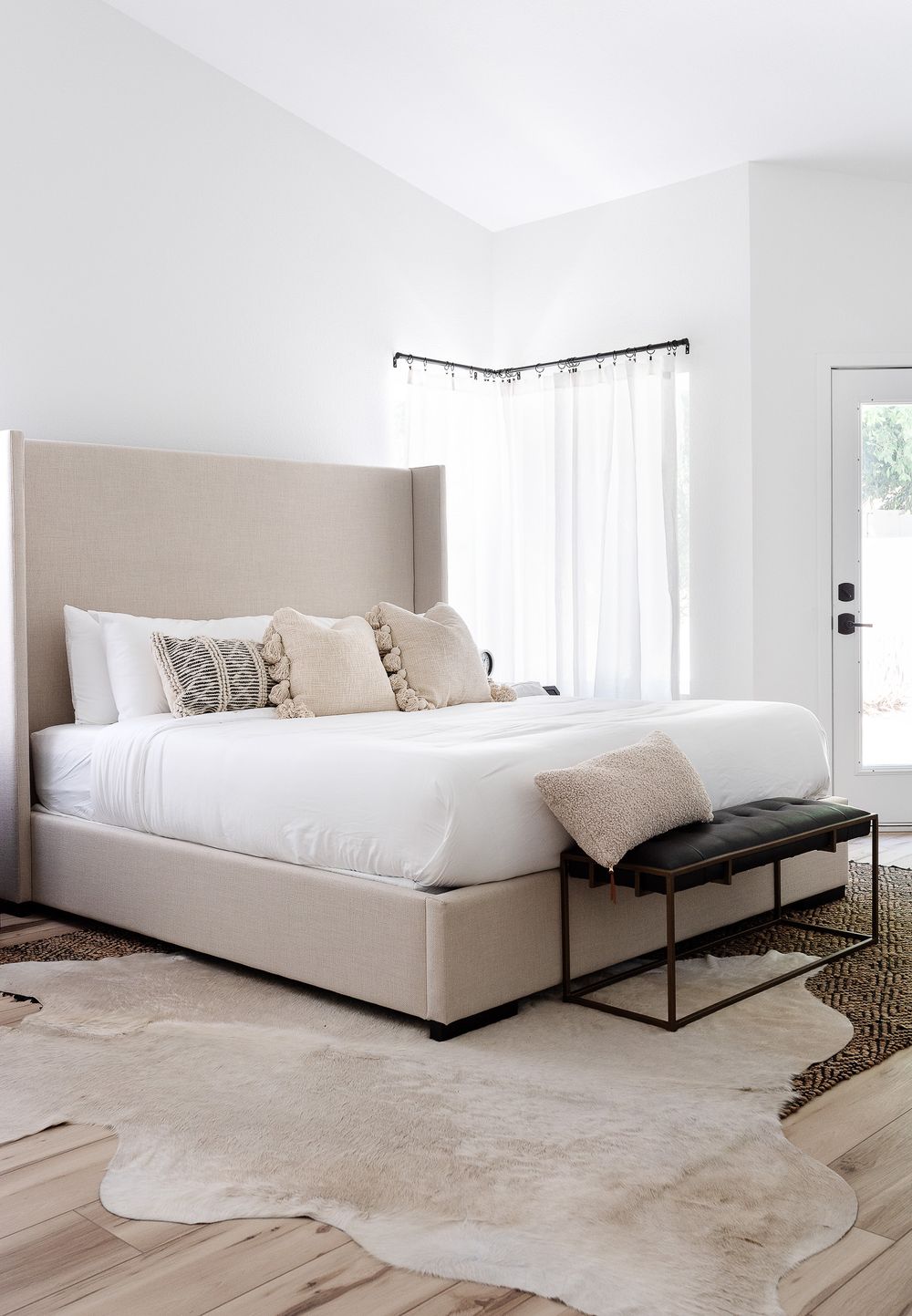 Modern bedroom featuring a beige upholstered bed, white bedding, and decorative pillows against bright white walls.