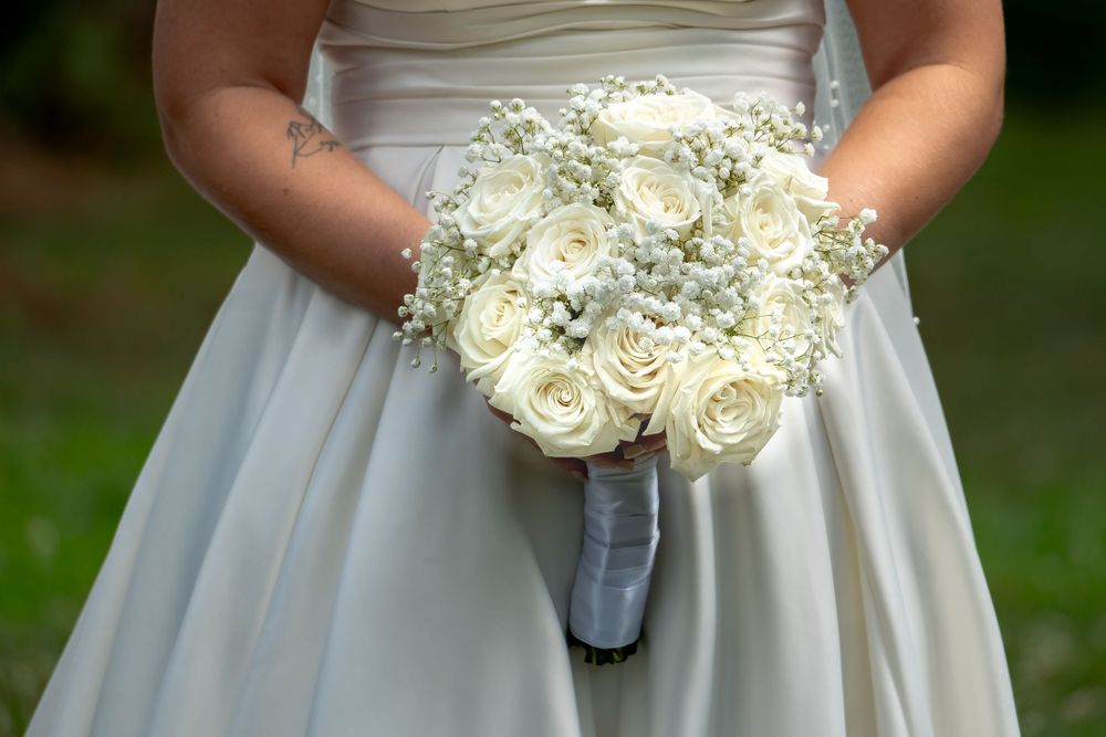 An elegant white rose and baby's breath wedding bouquet held against a light gray dress.