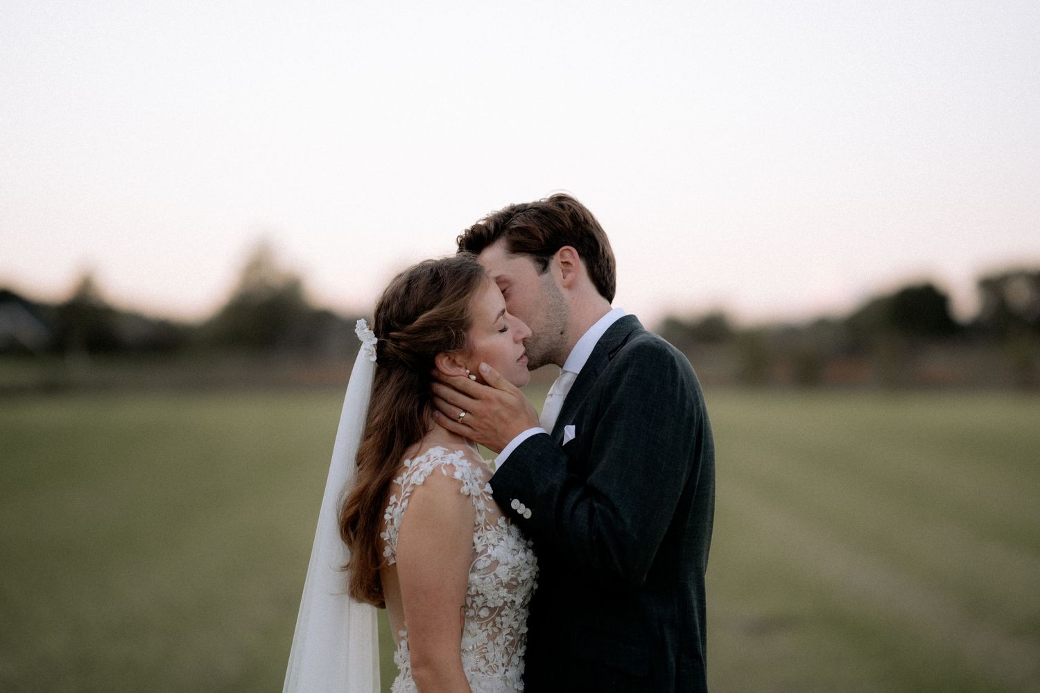A blissful wedding couple embracing in a picturesque countryside setting, surrounded by nature's beauty.