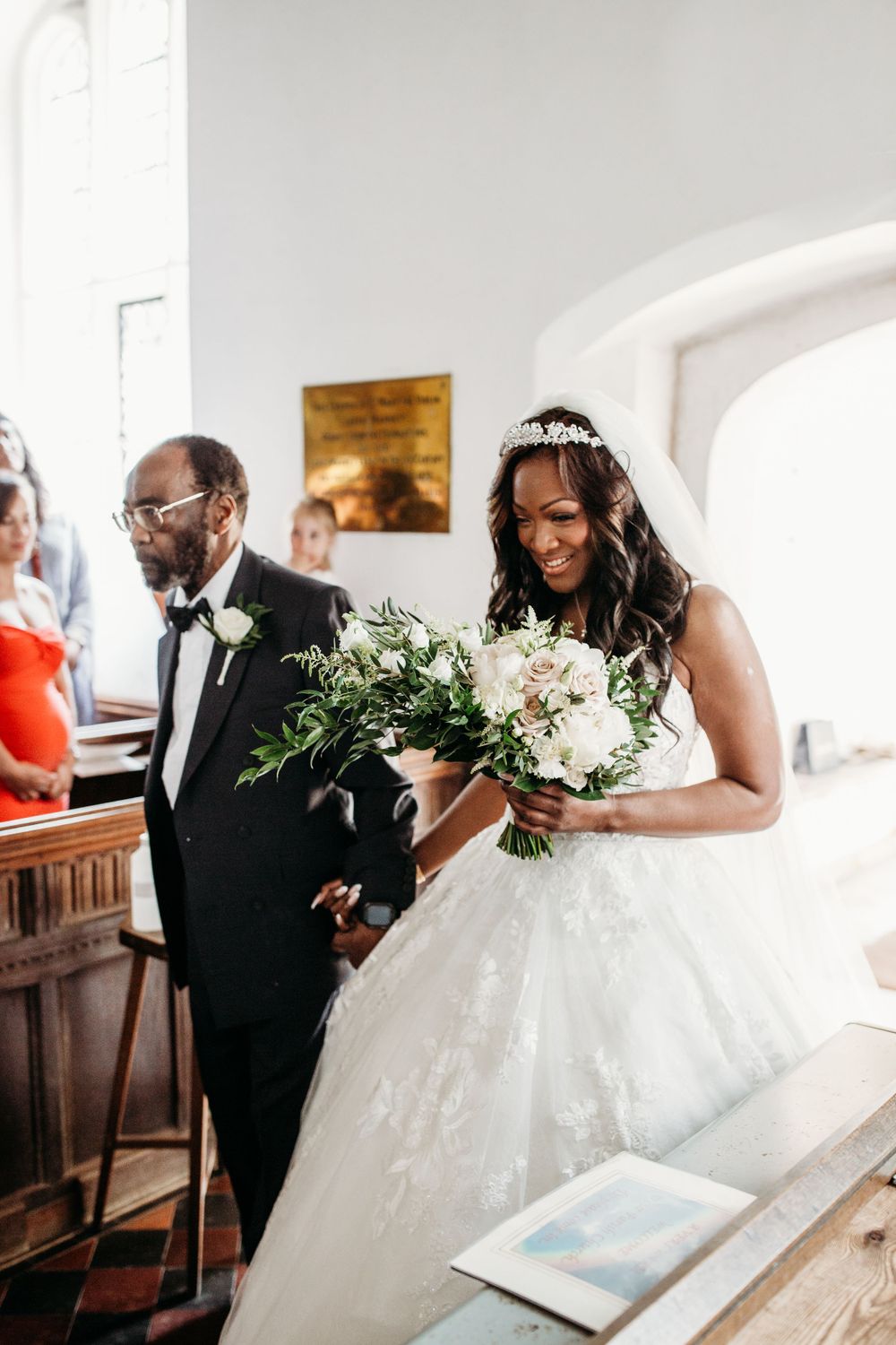 A bride in a traditional white gown carries a natural green and white bouquet during ceremony Layer Marney tower wedding