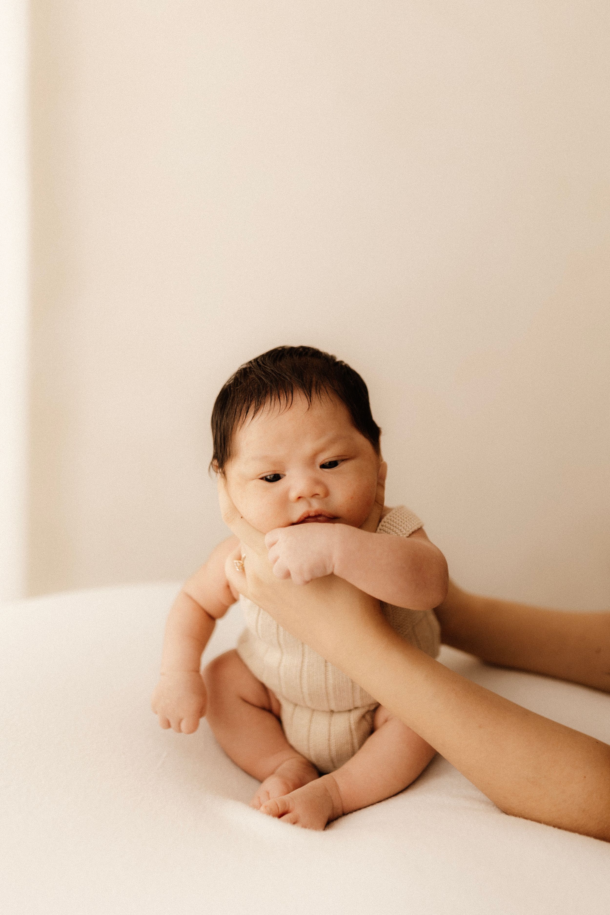 Baby in ribbed onesie held by caring hands against white background.