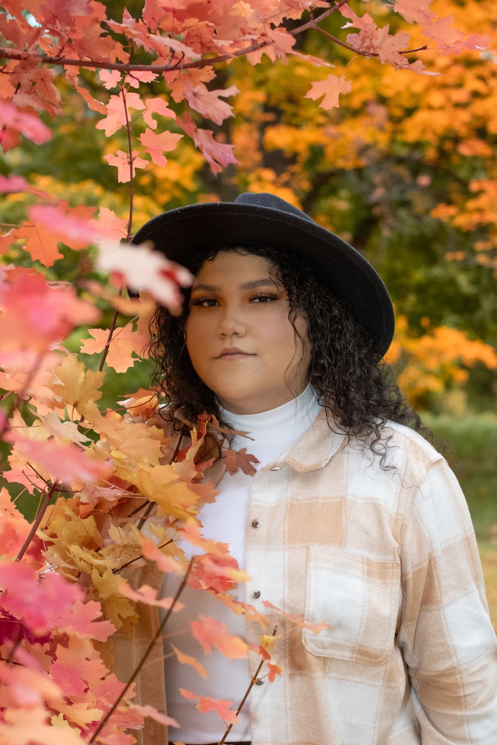 Autumn portrait with black hat against vibrant orange and pink fall foliage.
