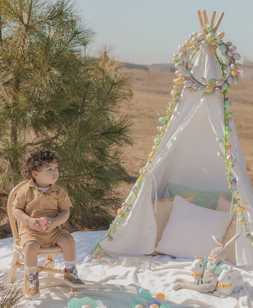 Boho desert photoshoot featuring small teepee decorated with flowers and cozy pillows.