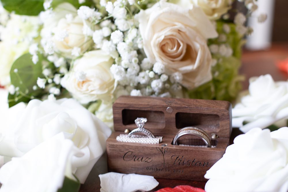 Wedding rings in a wooden box surrounded by white roses and baby's breath flowers in an elegant bridal setting.