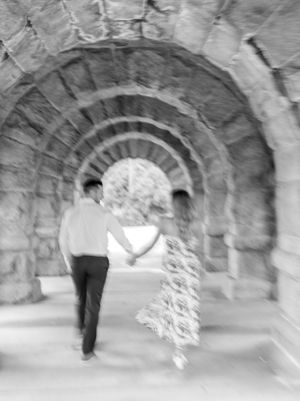 A couple walks through a stone archway tunnel creating an artistic black and white perspective.