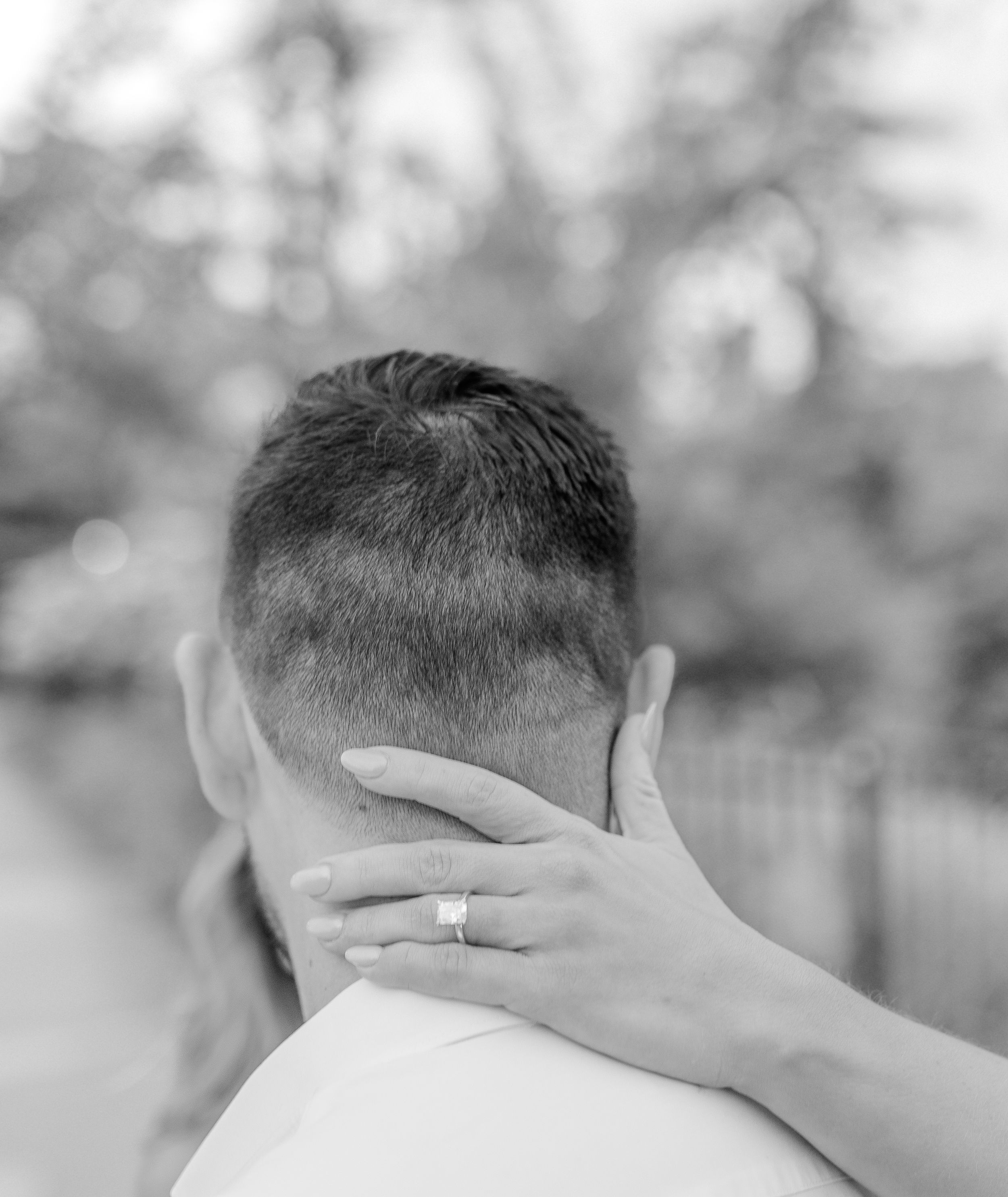 A close-up black and white photo showing hands embracing with a wedding ring visible.