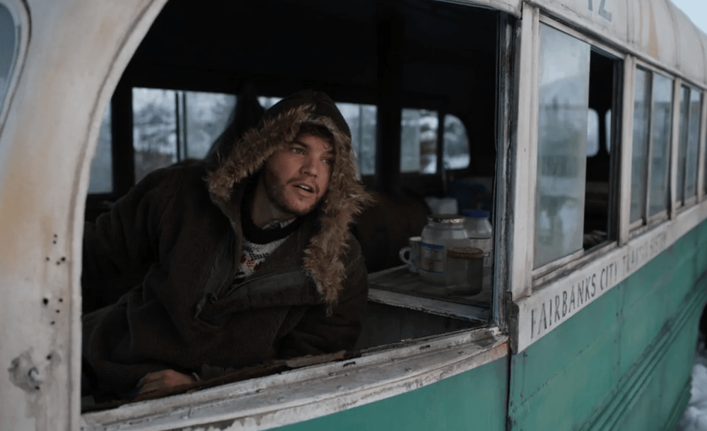 A vintage turquoise bus with travelers visible through windows on a mountain road.