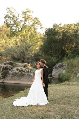 A romantic wedding couple sitting together on grass near rocky outcrops during golden hour.