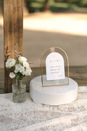 White decorative place cards and vases with flowers arranged on lace tablecloth.