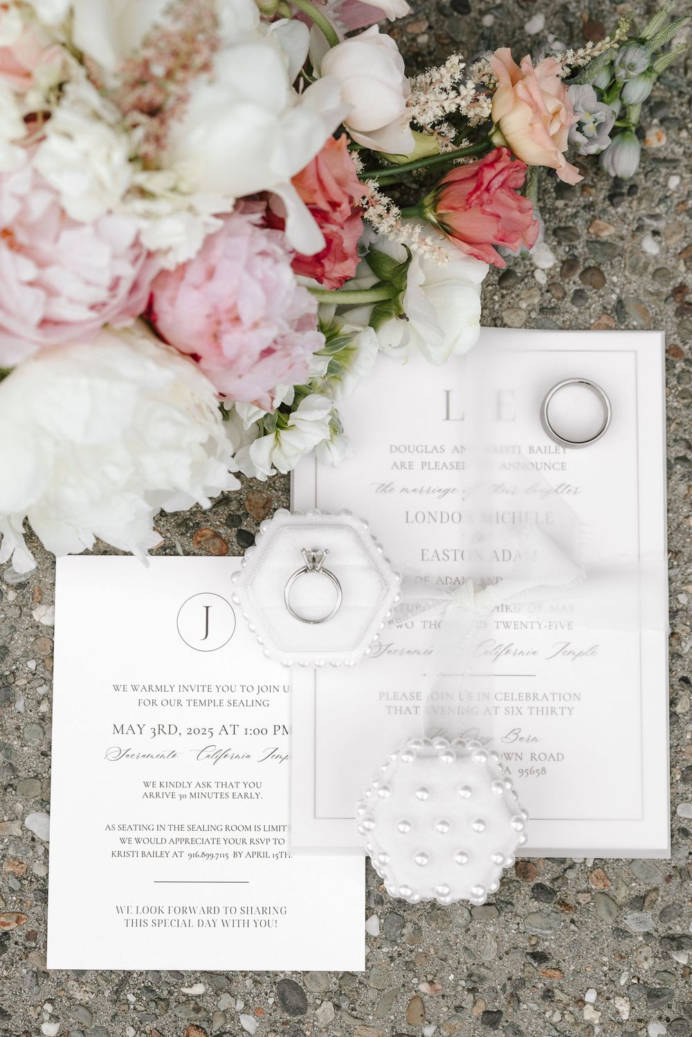 Elegant wedding invitations with white and pink floral arrangements displayed on textured stone background.