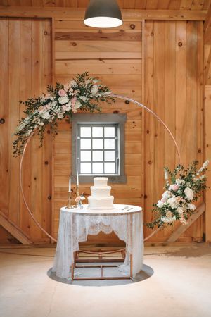 Rustic wooden barn venue decorated with white floral arrangements and a circular wedding arch setup.