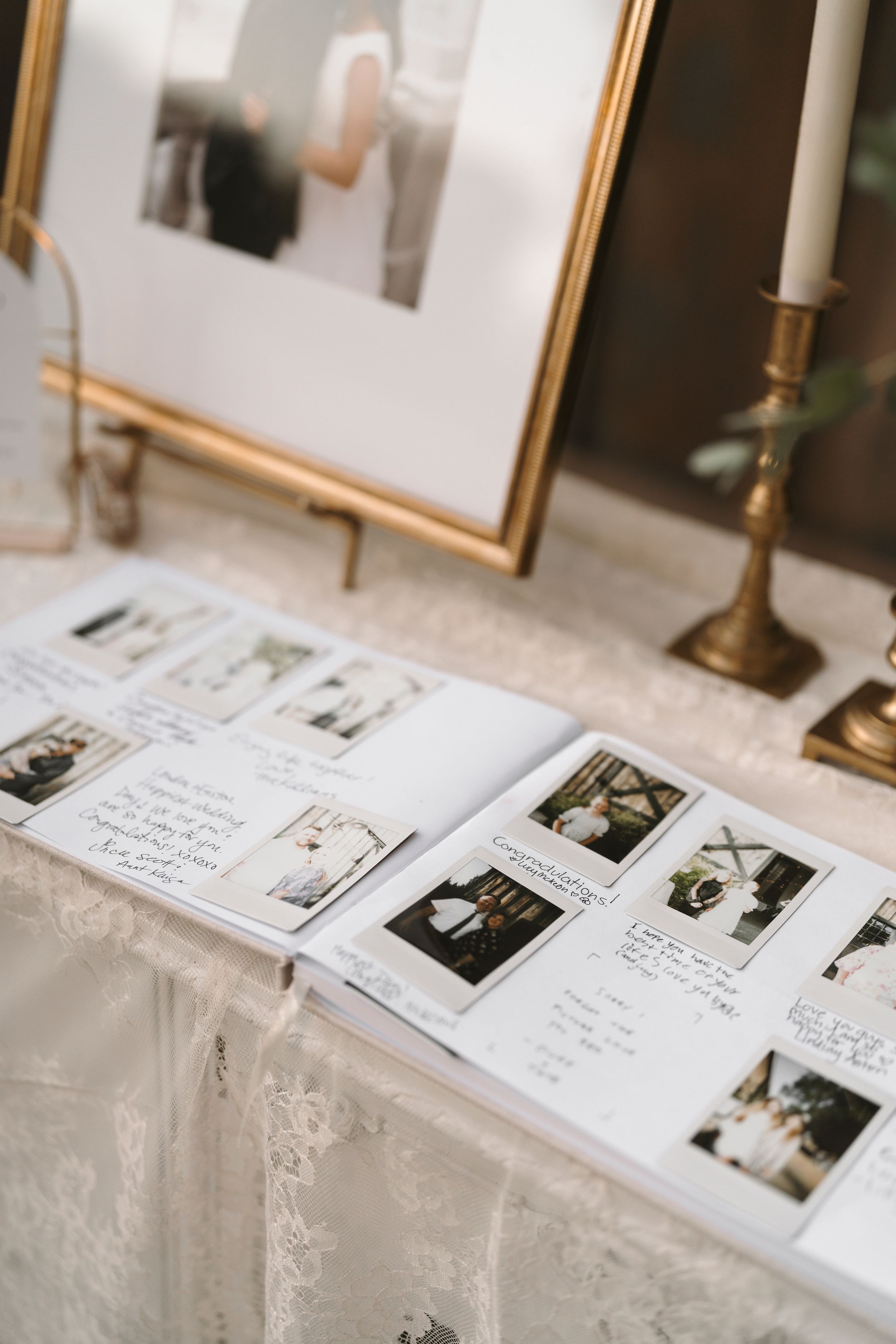 A guest book display at a wedding reception with polaroid photos and handwritten messages on white linen tablecloth.