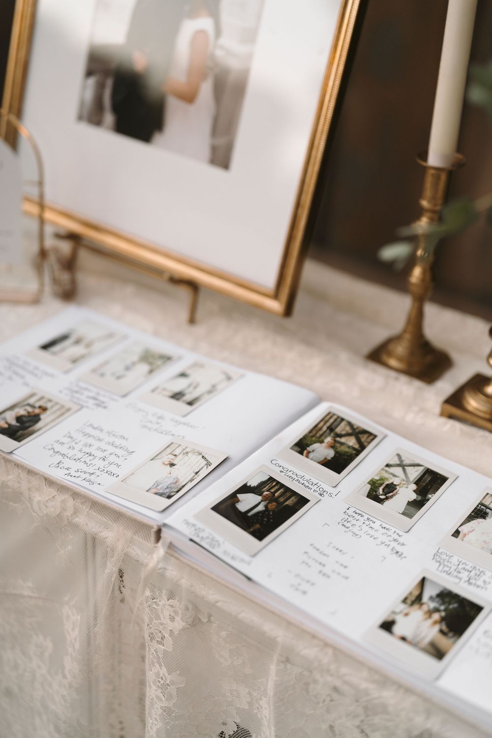 A guest book display at a wedding reception with polaroid photos and handwritten messages on white linen tablecloth.