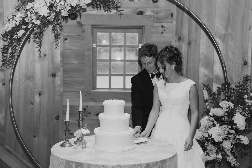 Three tiered white wedding cake on rustic wooden table in a cabin-style venue.