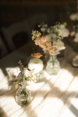 Small glass bud vases with delicate flowers and foliage create romantic table settings in natural sunlight.