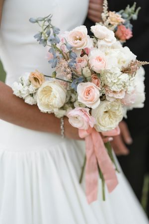 Romantic bridal bouquet featuring blush pink roses, white peonies and dusty blue accents tied with silk ribbon.
