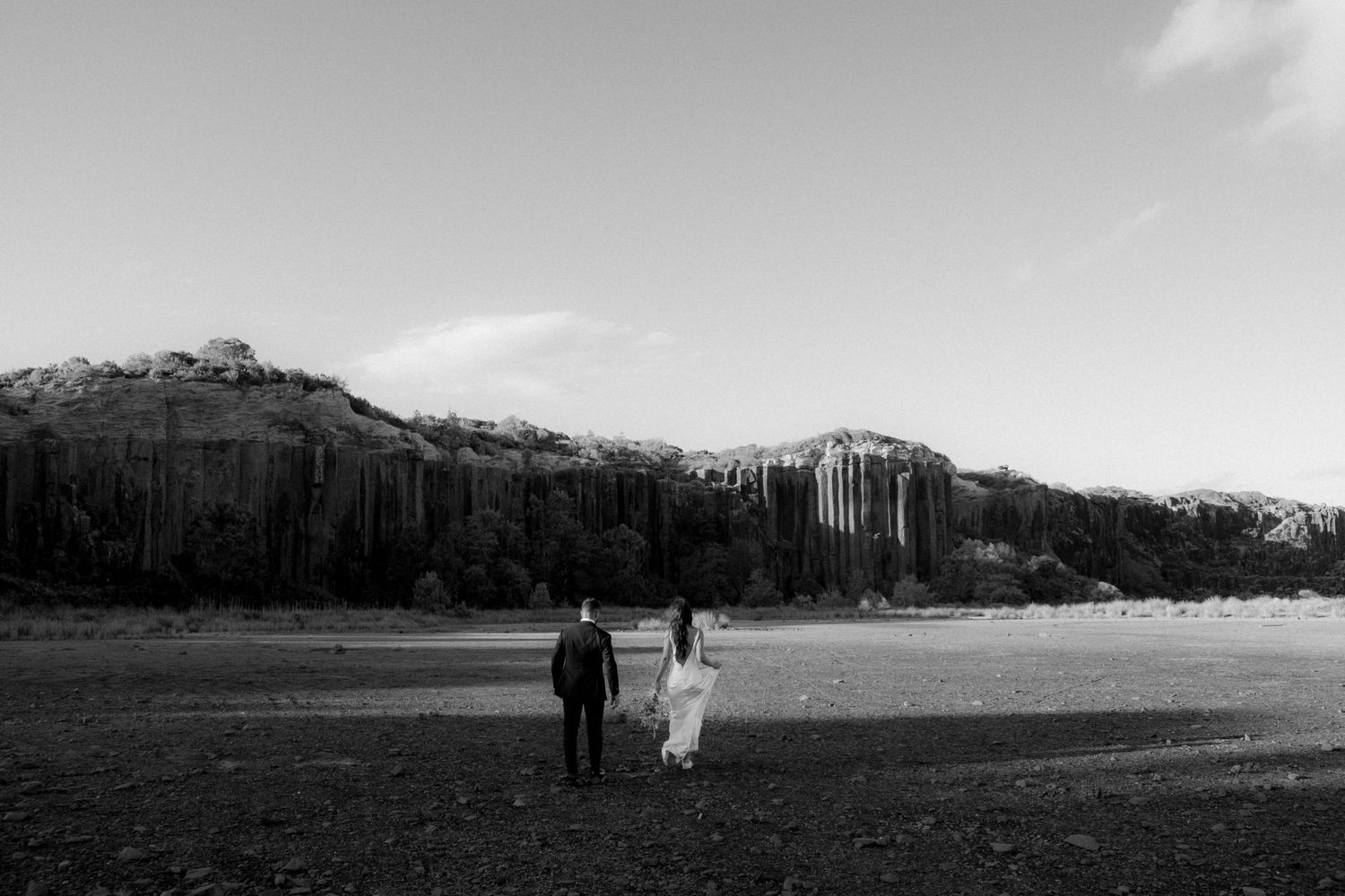 A couple walking together across a scenic field with mountains and trees in the distance.