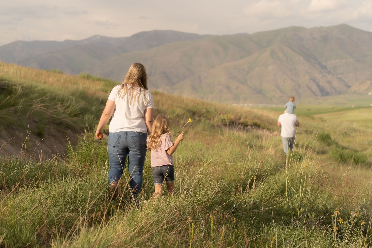 Family of four walking in the big hills located in cache valley overlooking logan. While holding hands during golden hour family session.