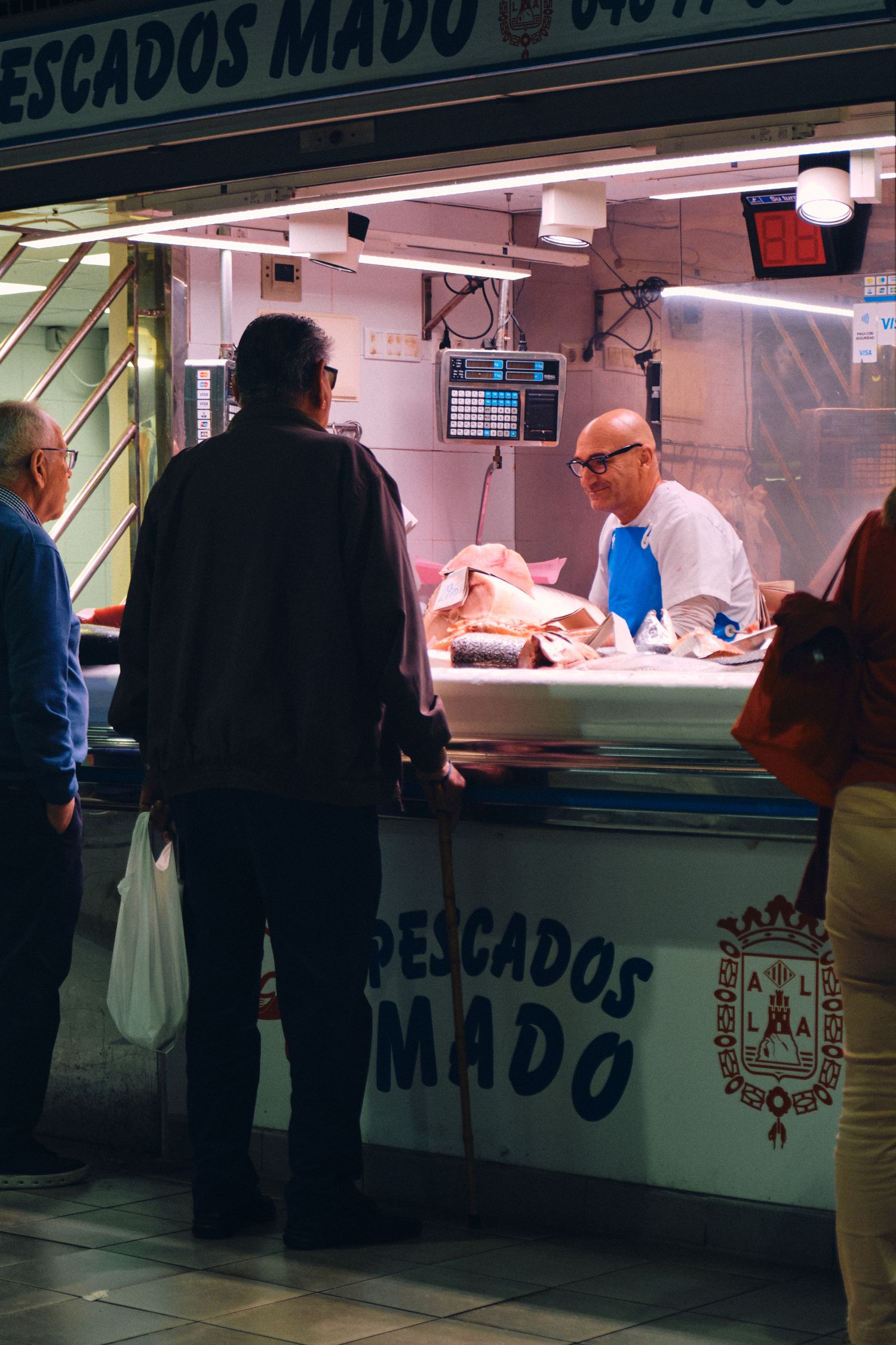 Customers at Pescados Mado fish market counter viewing fresh seafood.