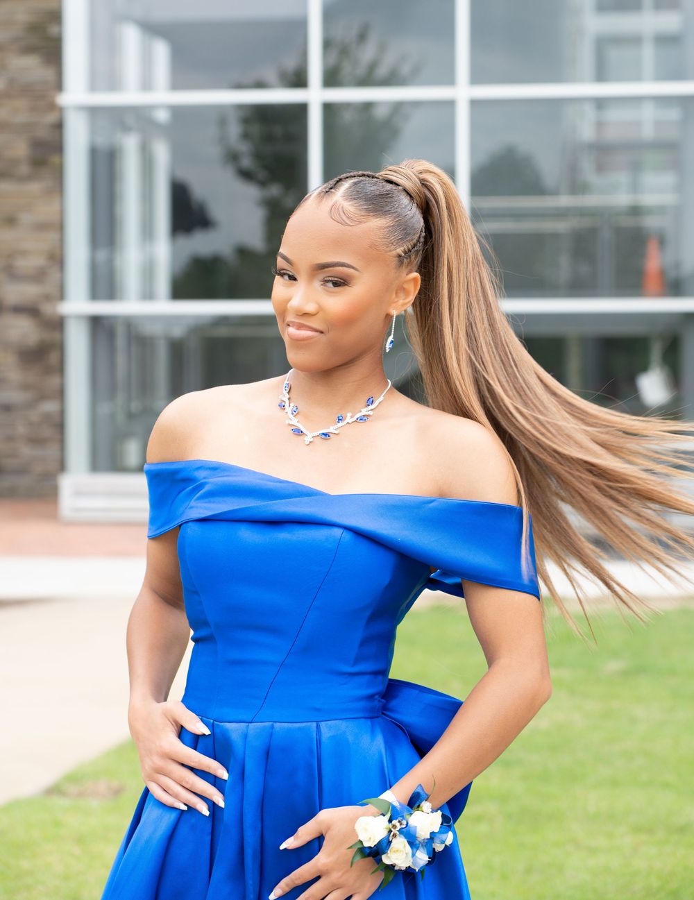Royal blue formal dress with off-shoulder design photographed in outdoor setting.