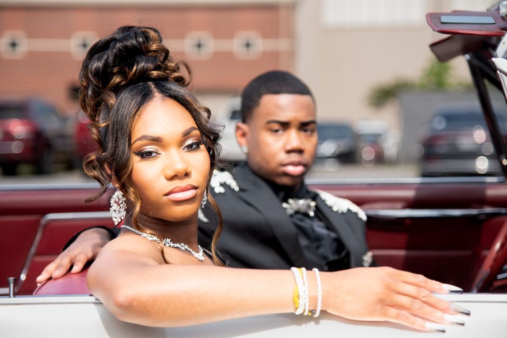 Elegant couple in formal wear posing near vintage car.