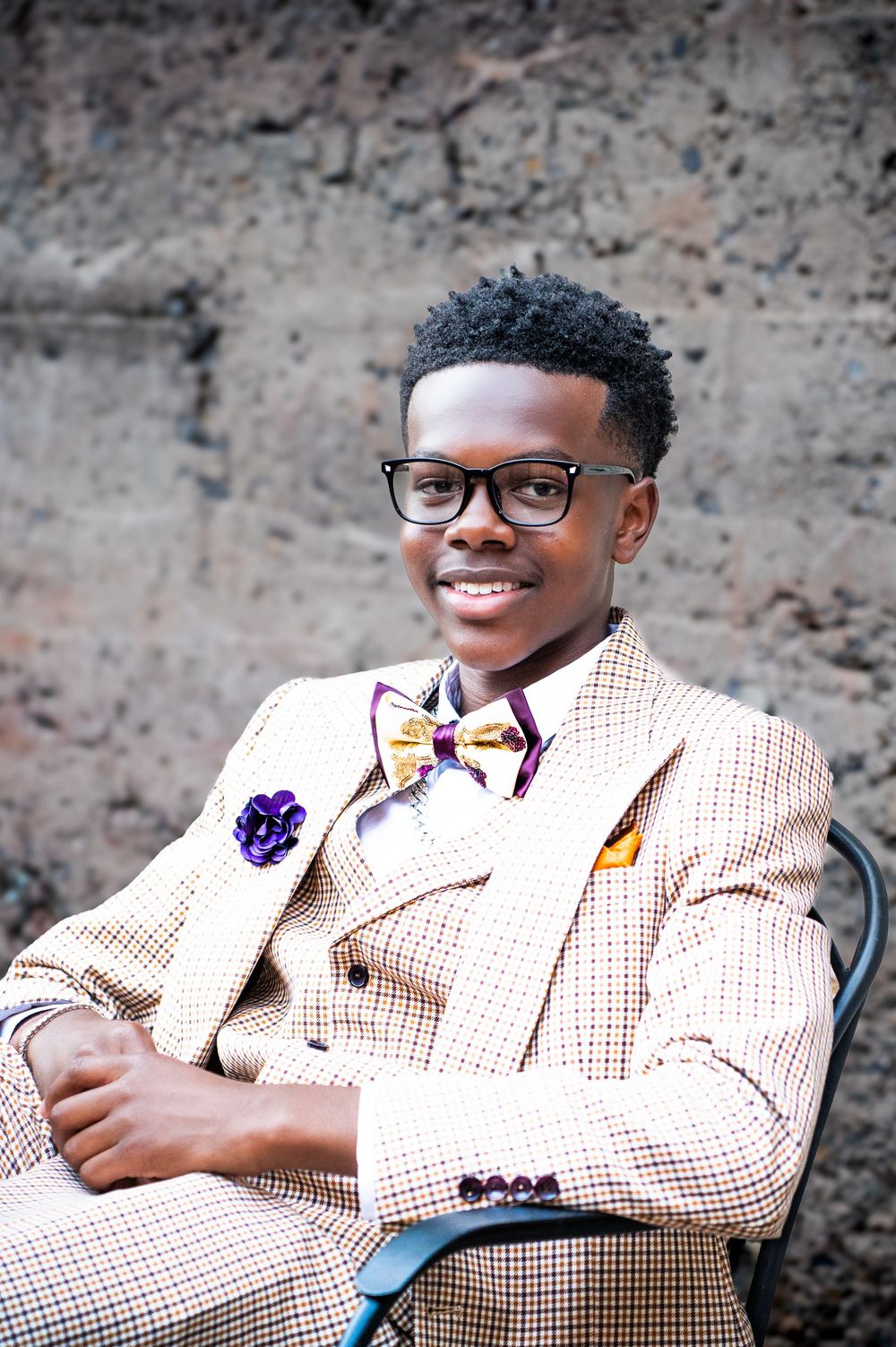 Professional headshots in beige checkered blazer against textured brick background.