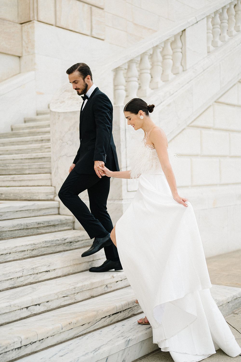 Bride in white gown and groom in black tuxedo hold hands while descending elegant marble staircase. - Detroit Institute of Arts Wedding
