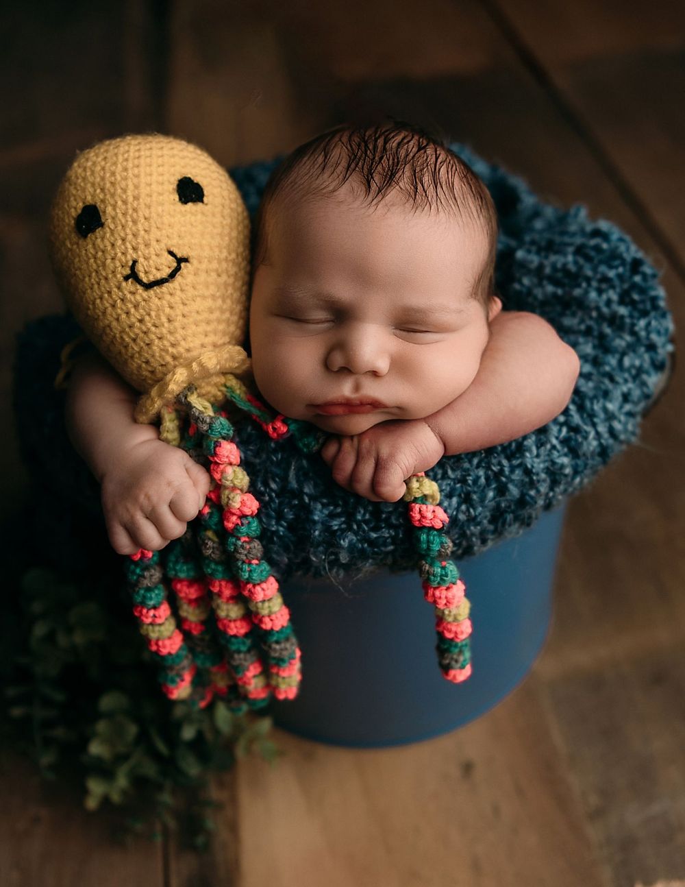 Sleeping newborn cuddled with yellow crocheted octopus toy on blue blanket.