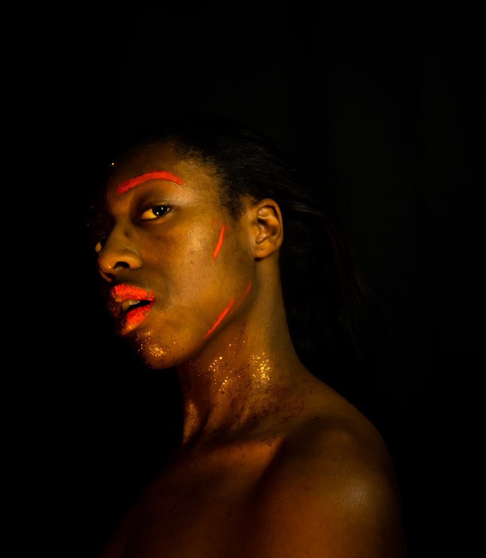 A person with orange paint on their face and gold glitter looking at the camera.