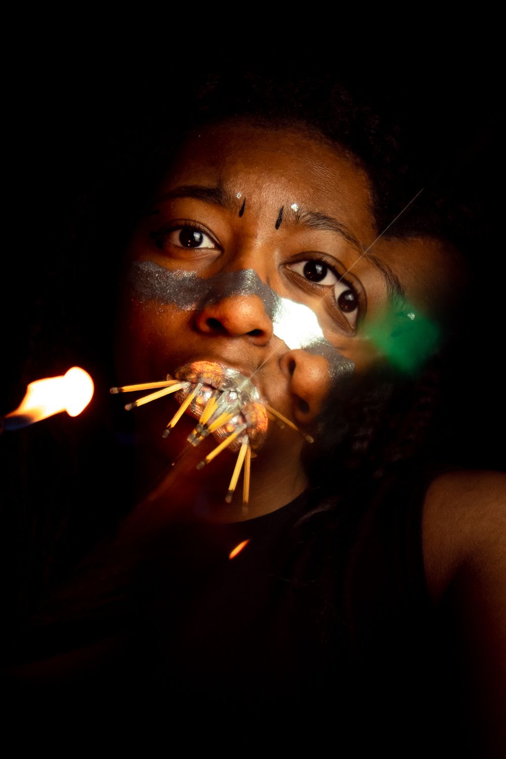 A person with matches in their mouth, fire on the left side, and reflection of part of their face on the right side.