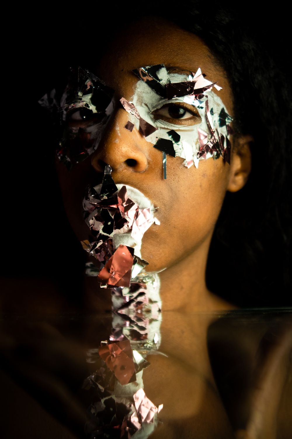 A person looking at the camera with paint and big glitter on their face, a small reflection near the bottom.