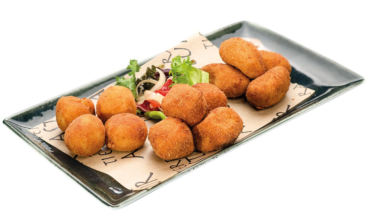 Croquetas doradas fritas dispuestas en un moderno plato rectangular negro con guarnición fresca. Tierra Astur
