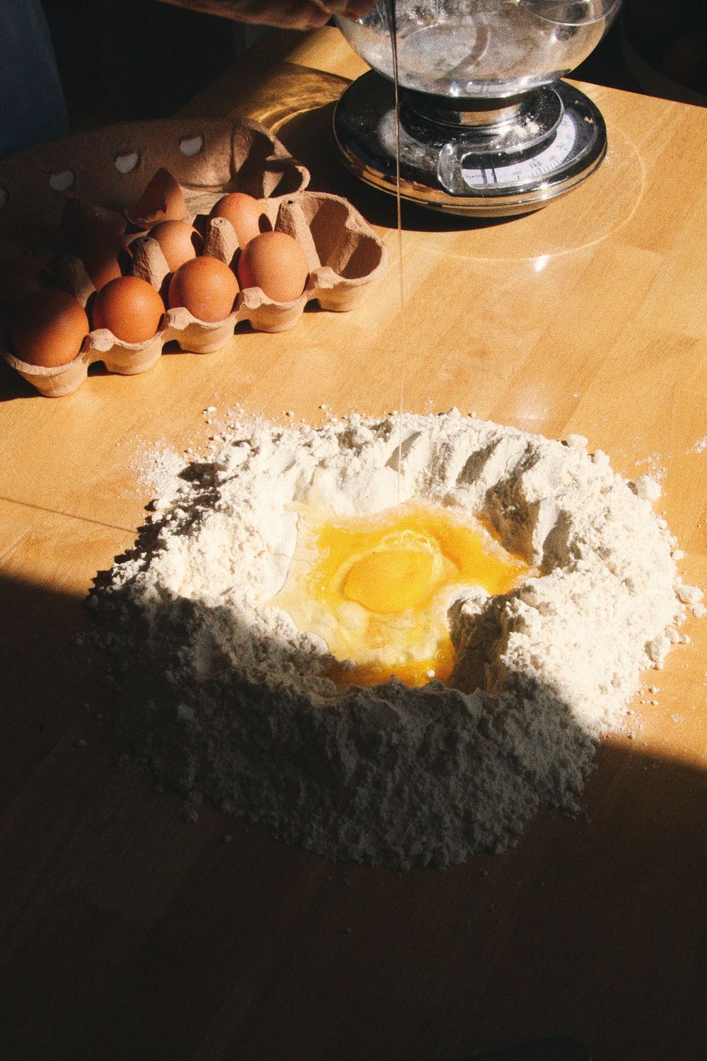 Flour with raw egg being mixed on a wooden cutting board in direct sunlight.