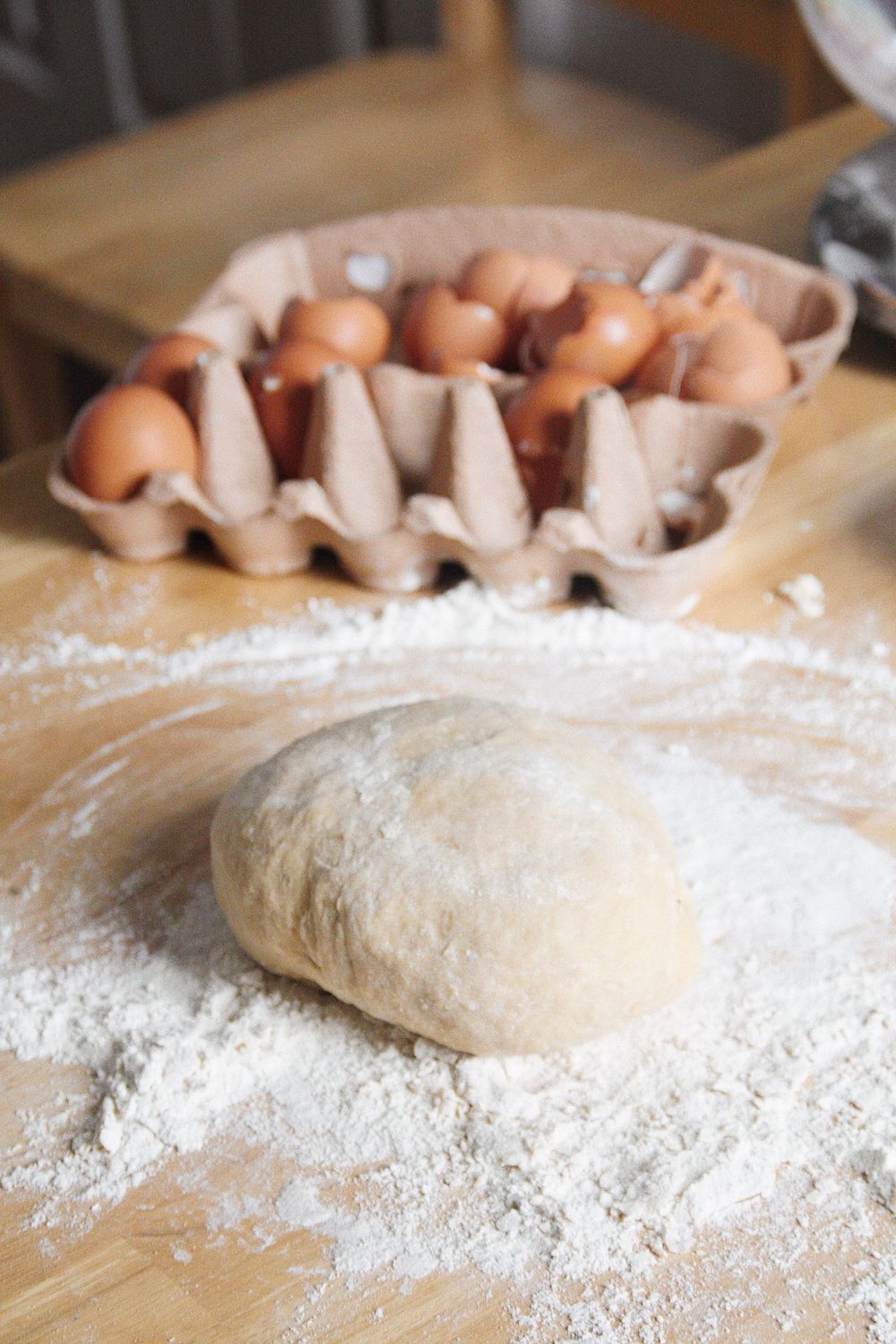 Raw bread dough being prepared on a floured surface next to brown eggs in cartons.
