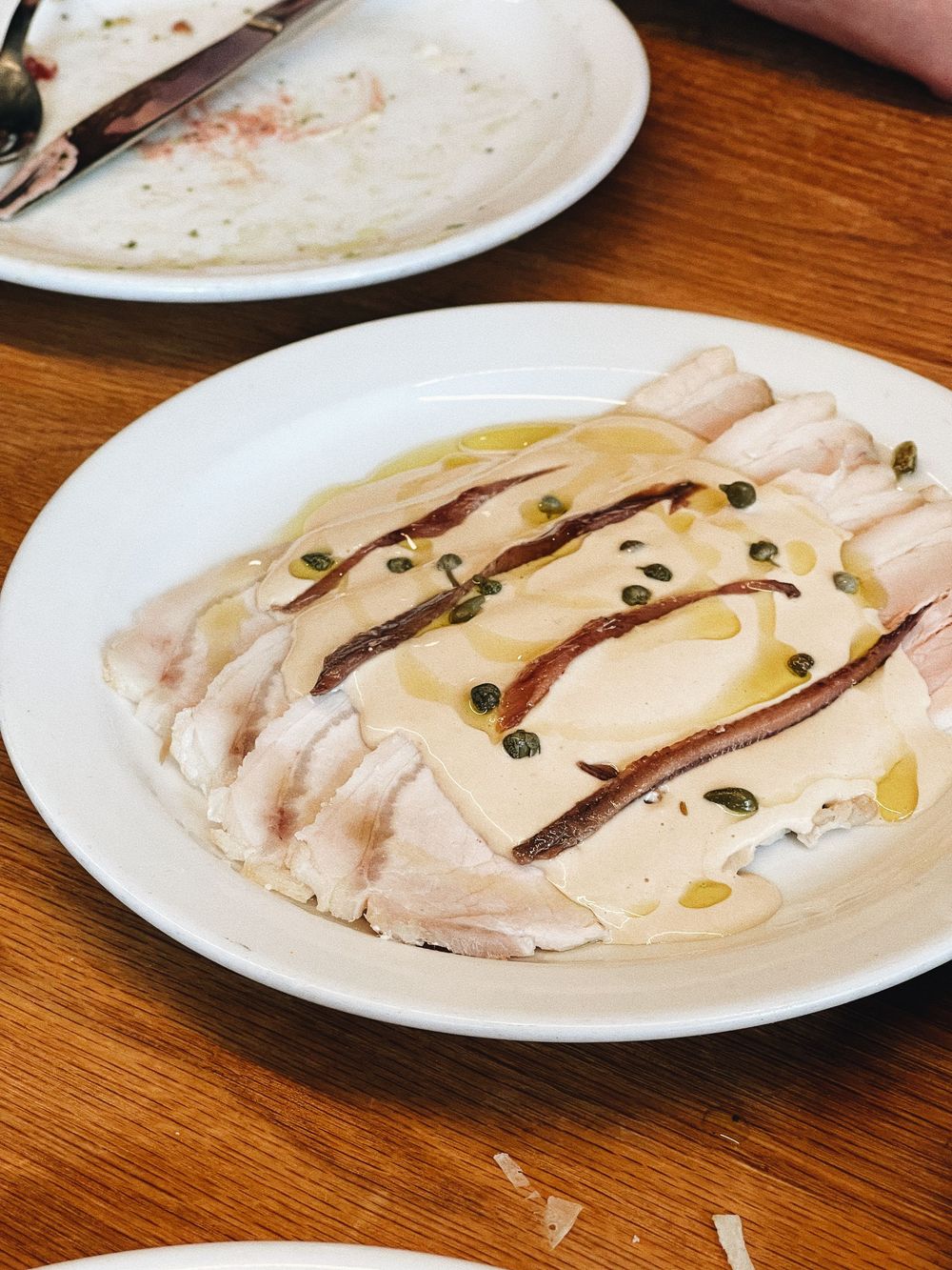 Sliced poached chicken breast drizzled with olive oil and garnished with black capers on a white plate.