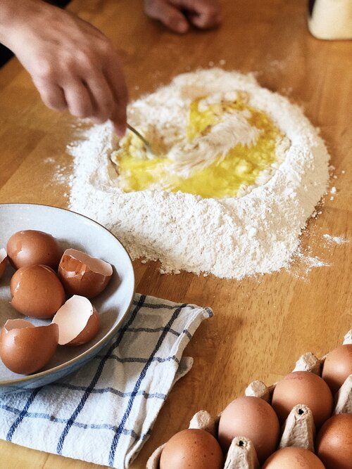 Raw eggs and flour arranged for making pasta dough on a wooden surface.