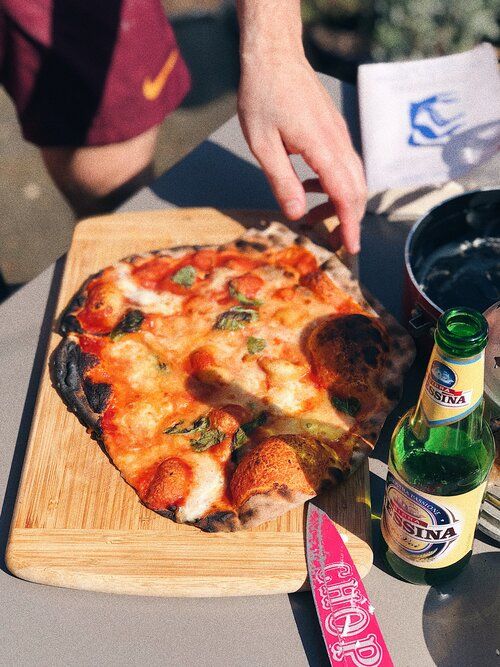 Homemade pizza on wooden board with melted cheese and bottles of beer nearby.