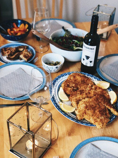 Breaded cutlets served on decorative plates with lemon wedges and wine glasses on a wooden dining table.