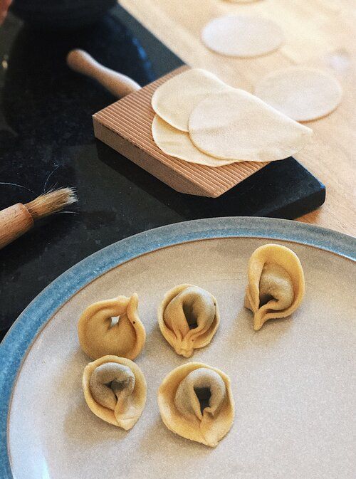 Handmade dumplings being shaped and arranged on a white plate showing the folding process.