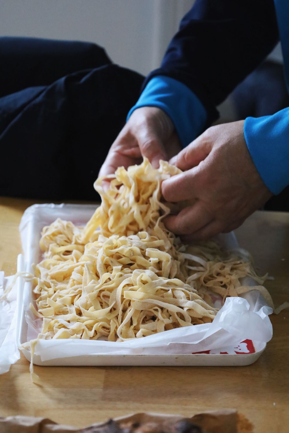 Fresh homemade pasta noodles being handled and separated on white parchment paper.