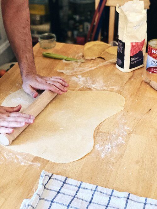 Rolling out fresh pasta dough on a floured wooden surface with a kitchen towel nearby.