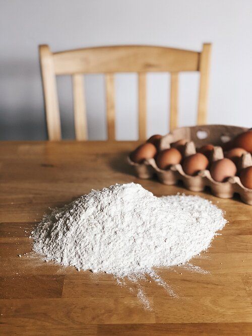 White flour piled on a wooden table with brown eggs in the background.