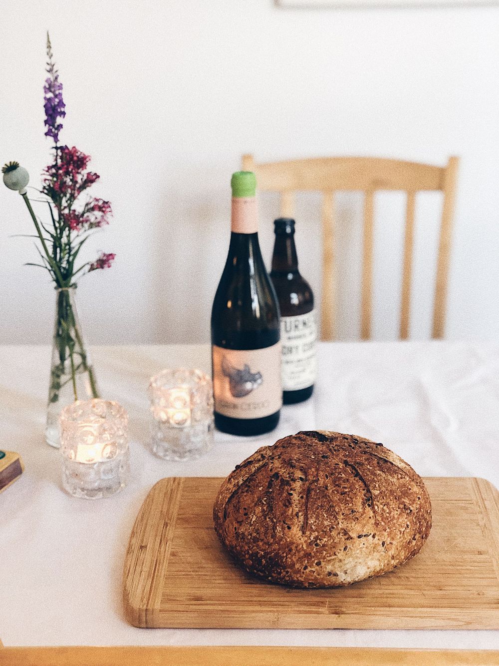 Rustic artisanal bread loaf on wooden board with wine bottles and candlelight setting.