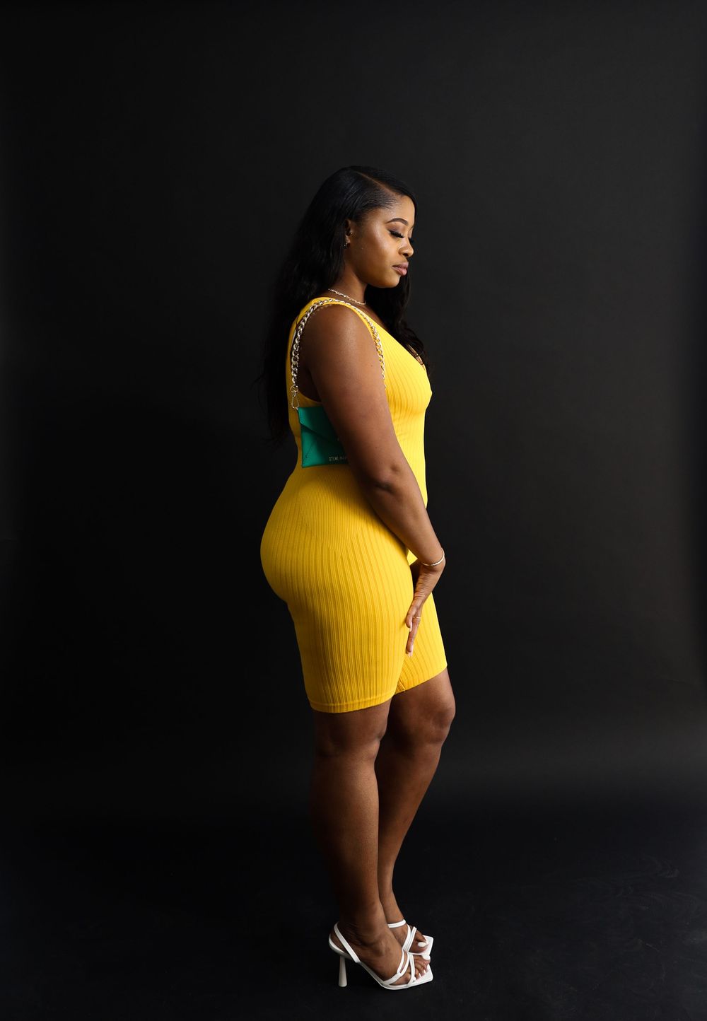 Side view of model in yellow fitted dress against dark background.
