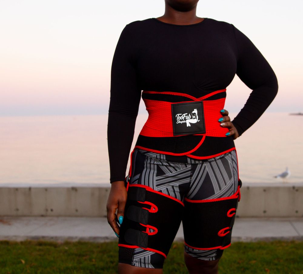 Person wearing black top and red waist trainer with graphic print shorts at sunset.