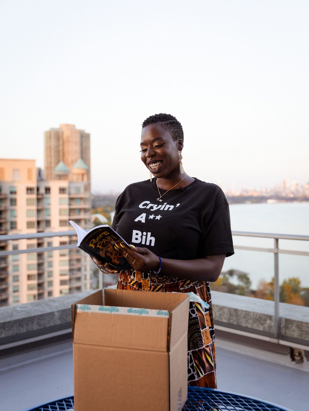 Person opening a package on a rooftop balcony with city buildings in background.