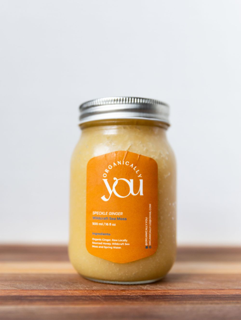 Glass jar of YOU organic smoothie with orange label on wooden surface.