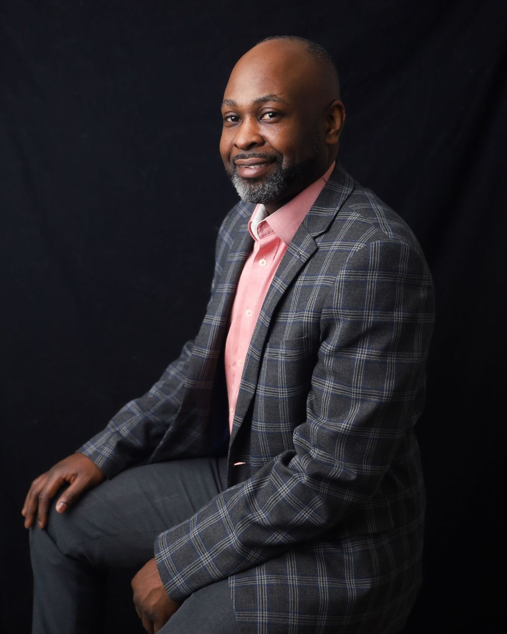 Professional portrait against dark background wearing plaid blazer and coral shirt.