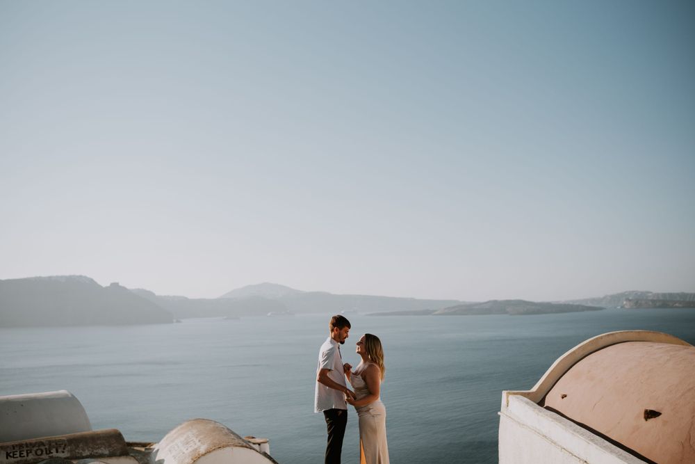 Intimate moment captured against backdrop of Aegean Sea and white domed buildings in Santorini.