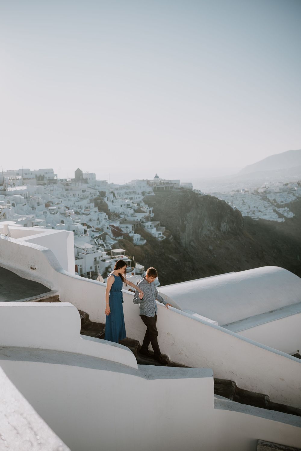 Romantic couple enjoying sunset views on white-washed steps in Santorini with traditional village in background.